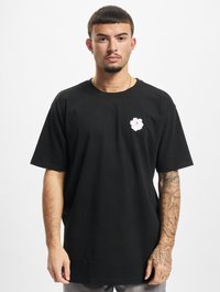 Sort bomulds T-shirt med en pink blomst broderet på venstre bryst, afslappet pasform og korte ærmer. Hudtekstur synlig på armene.