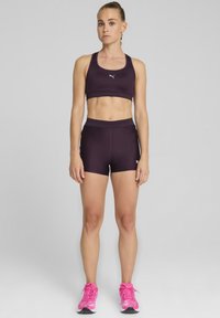 Lilla atletisk sportsbh og shorts, lavet af glat stof, parret med lyserøde løbesko. Har et logo på bh'en og shortsene.