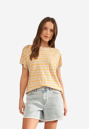 Femme portant un t-shirt à manches courtes rayé jaune et beige, associé à un short en jean taille haute bleu clair avec des ourlets effilochés.