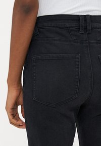 Mustat denimfarkut, joissa on korkea vyötärö, takataskut brodeeratulla yksityiskohdalla ja sileä pinta. Säädettävä vyötärön istuvuus.