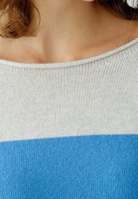 Sweter dziergany z wzorem w paski w kolorach kremowym, jasnoszarym i niebieskim. Szeroki dekolt typu łódka, miękka tekstura i prążkowane krawędzie.