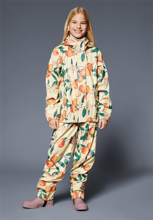 Imperméable jaune et pantalon avec des motifs de pêches et de feuilles ; le matériau est brillant et imperméable ; des bottes pourpres complètent l'ensemble.
