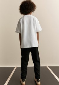 Hvid t-shirt med korte ærmer, parret med sorte bukser og lyse sko, med et enkelt design. Overfladen ser glat ud.