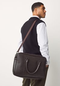 Braune Leder-Umhängetasche mit zwei oberen Griffen, einem abnehmbaren Schultergurt und einer glatten, strukturierten Oberfläche.