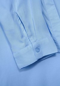 Poignet de chemise bleu clair à manches longues avec un bouton et une fente latérale sur la manche, montrant la texture détaillée du tissu.