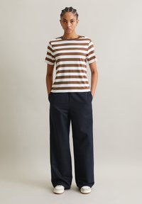 Striped t-shirt in brown and white, short sleeves, round neckline, paired with loose-fitting navy pants and white sneakers.