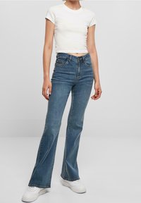 Blå högmidjade utsvängda jeans gjorda av denim. Har sömnadsdetaljer, femficksdesign och en ljus tvätt. Matchas med en vit topp med kort ärm.