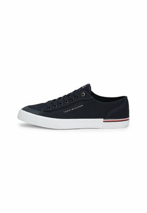 Zapatilla de lona marina con suela de goma blanca, puntera redonda, seis orificios para los cordones y logo distintivo. Presenta una franja de contraste en rojo y blanco en la suela.