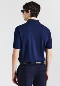 Polo navy con un design testurizzato, maniche corte e colletto. Abbinato a pantaloni scuri e una cintura nera.