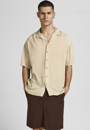 Camisa beige de manga corta con cuello con muescas, que cuenta con botones de madera, combinada con pantalones cortos marrones. Textura suave, corte relajado.