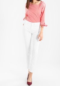 Rood en wit gestreepte blouse met driekwart mouwen en strikaccenten, gecombineerd met witte rechte broek en bordeauxrode hoge hakken.