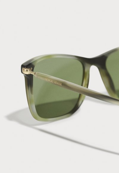 Žalios atspalvio saulės akiniai su skaidriu tamsiai žaliu rėmu ir auksinėmis detalėmis ant laikiklių, šone graviruotas "Giorgio Armani".