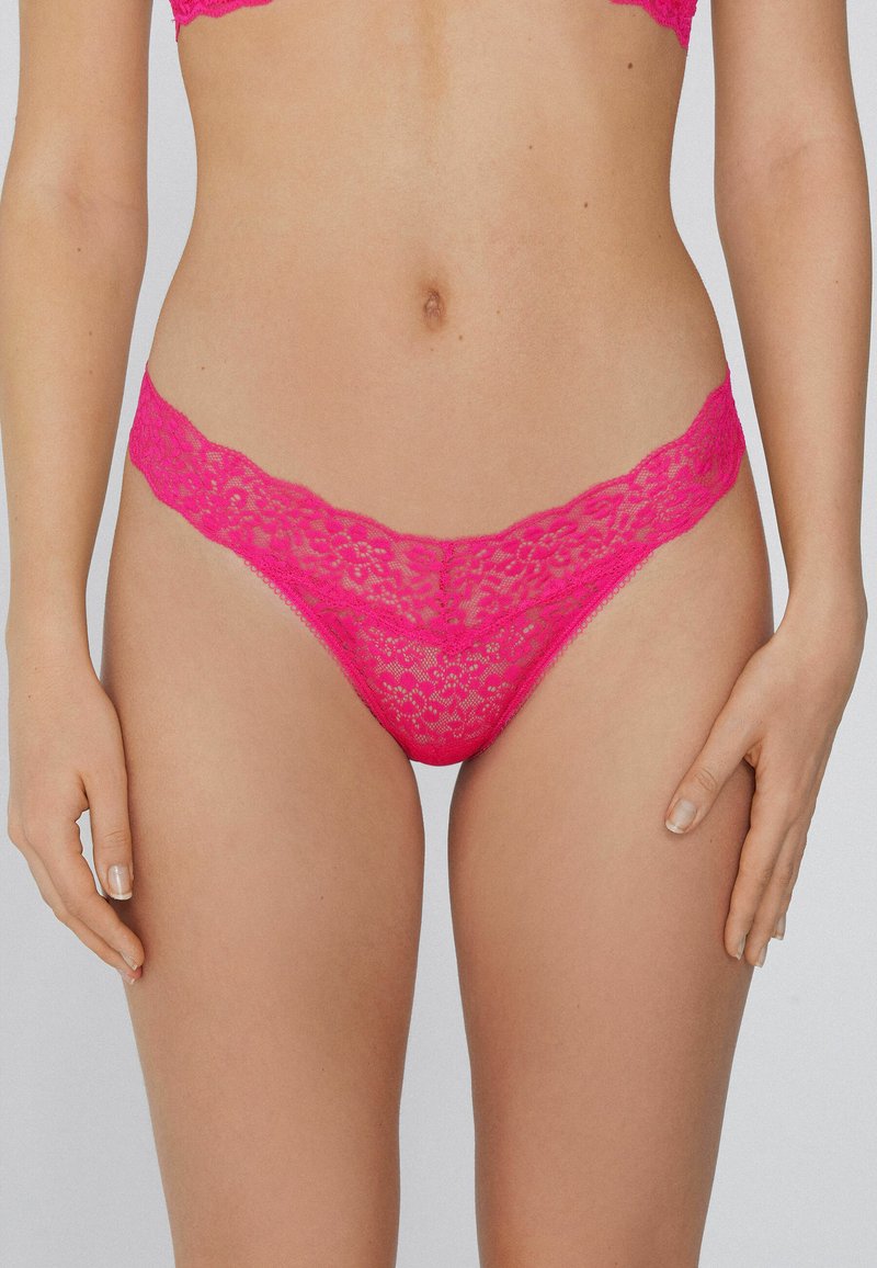 String en dentelle rose vif avec un motif floral, des bords festonnés et une texture délicate, offrant une couverture minimale et une finition douce.