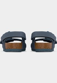 Ζευγάρι μπλε σανδάλια με ρυθμιζόμενους ιμάντες και ποδολεκάνες φελλού, εμφανιζόμενα από πίσω σε λευκό φόντο.