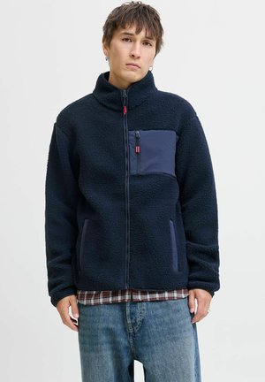 Marineblaue Fleecejacke mit hochgeschlossenem Kragen, Reißverschlusstasche auf der Brust und seitlichen Taschen. Strukturiertes Material mit kontrastierenden Paneldetails.