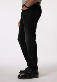 Jeans neri in slim fit con leggera scoloritura, realizzati in denim, dotati di tasche anteriori e posteriori, indossati con stivali in pelle nera.