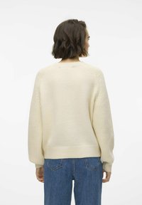 Maglione lavorato a maglia color crema con orlo a coste, vestibilità ampia e maniche testurizzate, abbinato a jeans in denim blu a vita alta.