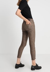 Leopardmönstrade byxor, bruna jeans med slim fit, femficksdesign och subtil blekning. Kombinerat med en svart ribbad tröja och svarta skor.