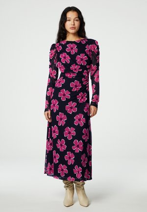 Langsleeve, marineblauwe jurk met een roze bloemenpatroon, gerimpelde schouders en een getailleerde silhoutte, gecombineerd met beige kniehoge laarzen.