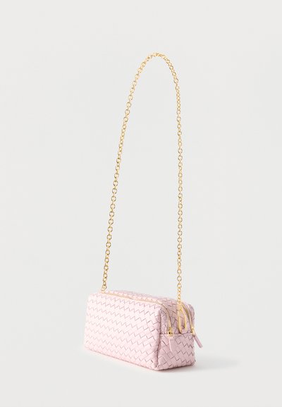 Μικρή ροζ υφασμένη δερμάτινη τσάντα με δύο χρυσά φερμουάρ και μακριά χρυσή αλυσίδα ιμάντα σε λευκό φόντο.
