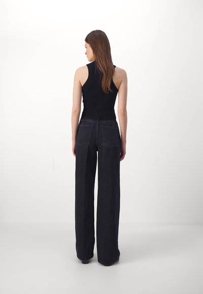 Débardeur noir à côtes associé à un jean noir à taille haute et jambes larges, avec poches arrière et une texture lisse.