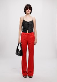 Black satin camisole with a front keyhole and button detail, paired with high-waisted, wide-leg red trousers and a black handbag.