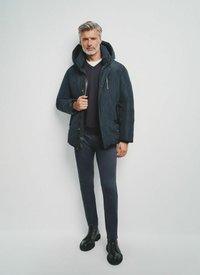 Ciemnoniebieska ocieplana kurtka puchowa z dużym kapturem, zapinana na zamek z przodu i z elastycznymi mankietami. Połączona z granatowymi spodniami o dopasowanym kroju i czarnymi butami z wiązaniem.