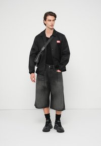 Μαύρο μπουφάν με κόκκινο λογότυπο, μαύρη μπλούζα, σκούρο γκρι τζιν σορτς και μαύρα αθλητικά παπούτσια. Τα αξεσουάρ περιλαμβάνουν μια μικρή τσάντα ώμου.