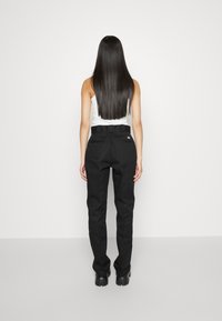 Black high-waisted trousers with a straight fit, belt loops, and two back pockets, paired with a white tank top. Smooth texture, minimal design.