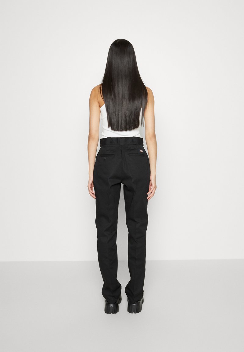 Pantalons noirs taille haute avec une coupe droite, passants de ceinture et deux poches arrière, associés à un débardeur blanc. Texture lisse, design minimal.