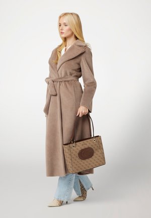 Cappotto in pelliccia sintetica marrone con vita regolabile, jeans svasati azzurri chiari e stivaletti alla caviglia beige in pelle di serpente. Borsa a tracolla marrone con motivo e logo.