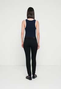 Body blu navy con rifiniture bianche, abbinato a jeans skinny neri. La modella si trova di spalle rispetto alla fotocamera, mettendo in risalto la vestibilità e i dettagli del design.