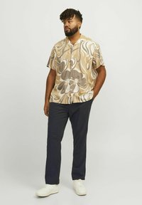 Camisa de manga corta con estampado en tonos beige y marrón, con diseños florales. Combinada con pantalones oscuros y ligeros y zapatillas blancas.