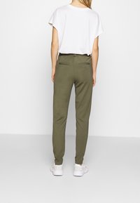 Olivgrüne Jogginghosen mit zwei Gesäßtaschen, die eine taillierte Silhouette und einen elastischen Bund aufweisen. Kombiniert mit einem locker sitzenden weißen T-Shirt.