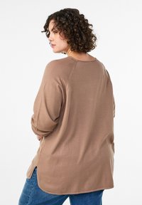 Hnedý voľný sveter s okrúhlym výstrihom, textúrovanou tkaninou a švami na ramene s miernym spustením. Bočné rozparky pre ľahší pohyb.