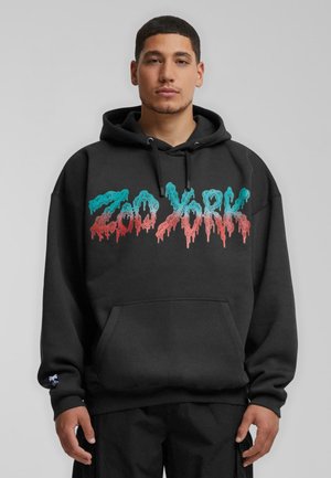 Schwarzer Hoodie mit vorderer Kängurutasche, mit buntem, tropfendem Text "Zoo York" in Türkis und Rot. Baumwollmaterial, lockere Passform.