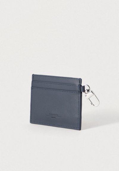 Θήκη καρτών από δέρμα σε ναυτικό μπλε χρώμα με τρεις θήκες και ασημένιο κλιπ εξαρτημάτων. Λείο υφή με διακριτικό λογότυπο στο μπροστινό μέρος. Συμπαγές ορθογώνιο σχήμα.