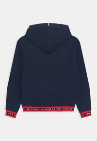 Felpa blu navy con cappuccio, rifiniture rosse sui polsini e sull'orlo, caratterizzata da un testo ripetuto "Tommy Hilfiger" in bianco.