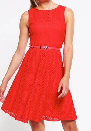 Rød kjole med ærmeløs design, der har et tekstureret perforeret stof og et solidt pink bælte i taljen, som flår ud ved kanten.