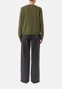 Zielona bluza z okrągłym dekoltem i ściągaczami na rękawach, zestawiona z szarymi, szerokimi jeansami z wysokim stanem i tylnymi kieszeniami.