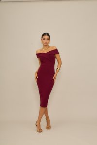 Κόκκινο μπουρντό φόρεμα με ακάλυπτους ώμους από ελαστικό ύφασμα, με εφαρμοστή γραμμή, μήκος μέχρι το γόνατο και διακριτική πιέτα. Συμπληρώνεται από χρυσά αξεσουάρ.