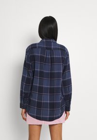 Camicia di flanella blu navy con un motivo a quadri in tonalità di blu e rosa, caratterizzata da un orlo leggermente curvo e maniche lunghe.