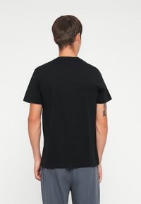 Black cotton t-shirt with short sleeves and a round neckline, displayed from the back. Features a smooth texture and minimal design.