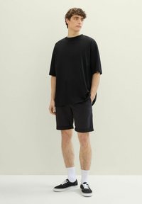 Czarny oversized t-shirt, czarne zwijane szorty, białe skarpetki i czarne sneakersy. Gładki materiał i luźny krój z krótkimi rękawami.