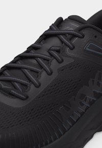 Κοντινή λήψη μαύρου αθλητικού παπουτσιού με λεπτομερή υφή υφάσματος, μαύρα κορδόνια και διακριτικές μπλε πινελιές στη σόλα και στο λογότυπο στο πλάι.