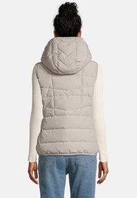 Puffy, lichtgrijze vest met een hoge kraag en capuchon, voorzien van een gewatteerd patroon en geribde mouwen, gecombineerd met lichtblauwe jeans.