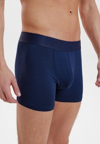 Marinblå bomullskalsonger med en strukturerad midja som har präglade bokstäver. Sittande design, jämn textur och midjehöjd.