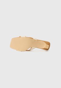 Square-toed heel sandal with a tan sole. Features cross-over cream straps and a low block heel. Textured bottom surface for grip.