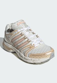 Balta sporta apavi ar bēšiem akcentiem un fakturētu acs virsmu. Tajos ir mīkstināta zolīte, izteiksmīga kurpju auklu sistēma un logotipa detaļa.