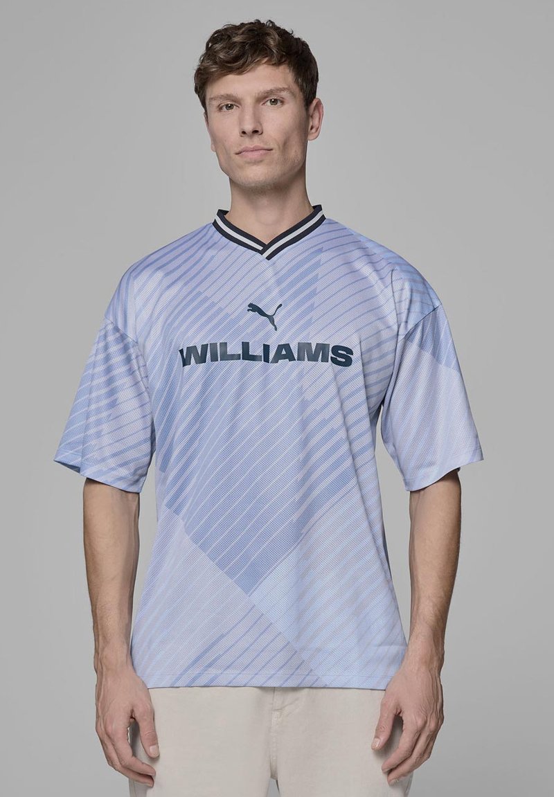 Jasnoniebieski, krótko rękawowy t-shirt z ukośnymi paskami, czarnym kołnierzykiem i napisem "WILLIAMS" wytłoczonym dużą, ciemną czcionką na klatce piersiowej.